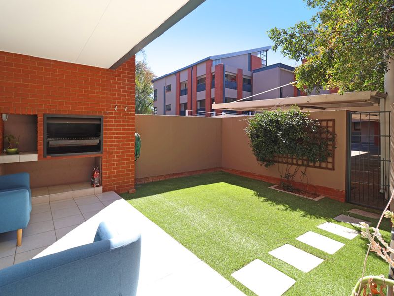 A covered patio area featuring a built-in braai, tiled flooring, and a private garden space with artificial lawn and boundary wall.