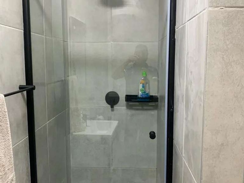 Modern walk-in shower featuring grey wall tiles, a black-framed glass screen, and a contemporary rain shower head.