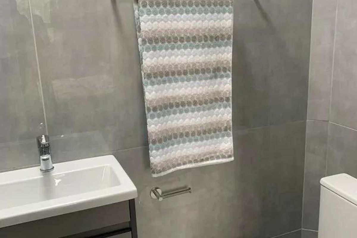 A modern bathroom featuring grey wall tiles, a sleek vanity cabinet with a basin, and a white toilet.