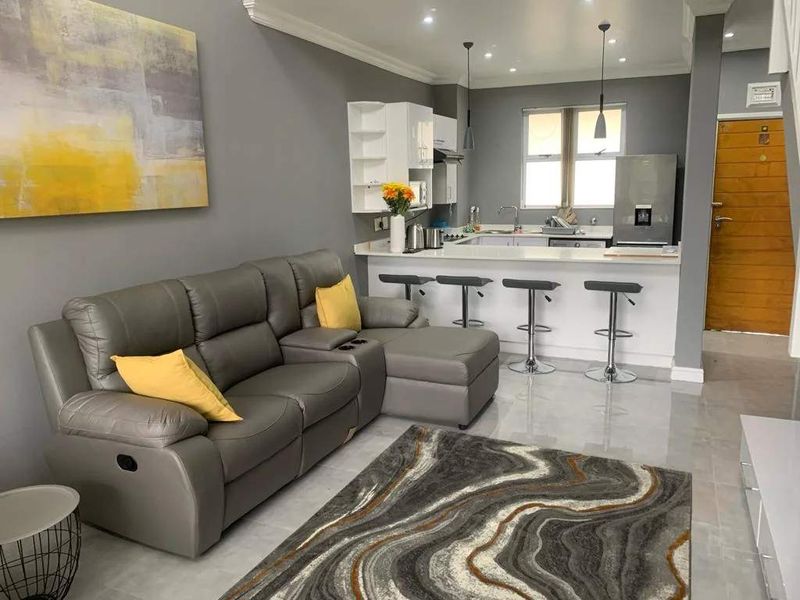 Modern open-plan living area featuring a well-appointed kitchen with breakfast bar, sleek cabinetry, and tiled flooring throughout.