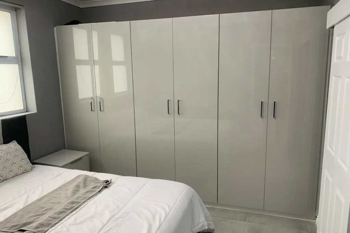 A well-maintained bedroom featuring modern high-gloss built-in cupboards, neutral grey walls, and clean tiled flooring.