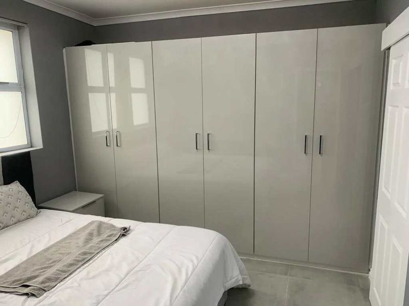 A well-maintained bedroom featuring modern high-gloss built-in cupboards, neutral grey walls, and clean tiled flooring.