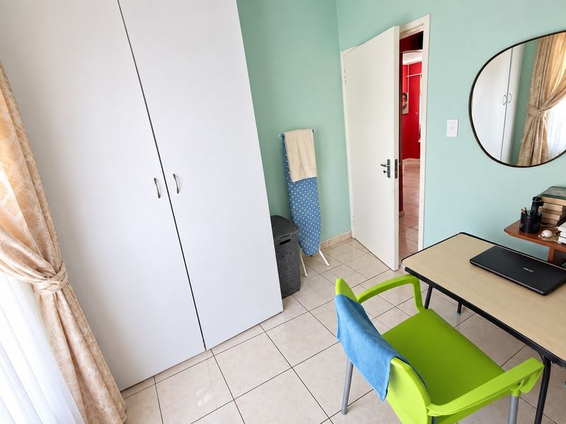 A bedroom featuring light green walls, tiled flooring, and a built-in white wardrobe, providing a functional and neutral living space.