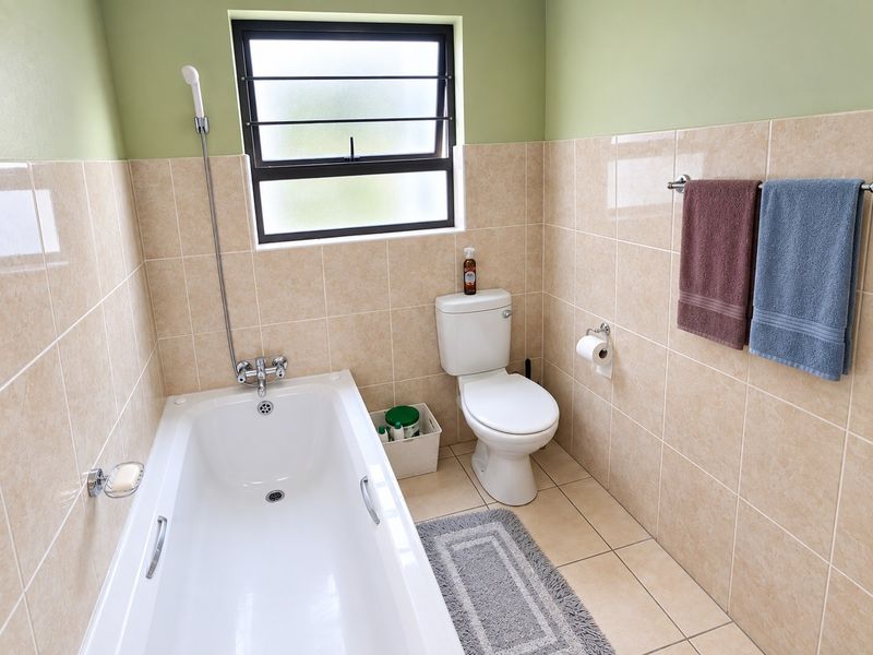 A functional bathroom featuring a bathtub with a handheld shower mixer, a standard toilet, and neutral wall and floor tiling.