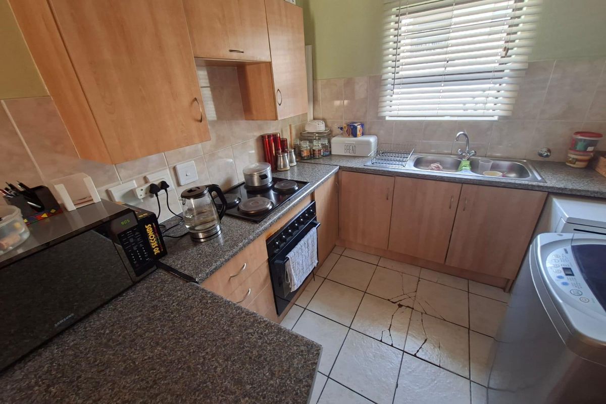 A functional kitchen featuring wood-finish cabinetry, granite countertops, a built-in oven and hob, and a double basin sink with tiled flooring.