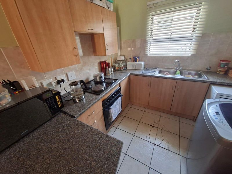 A functional kitchen featuring wood-finish cabinetry, granite countertops, a built-in oven and hob, and a double basin sink with tiled flooring.
