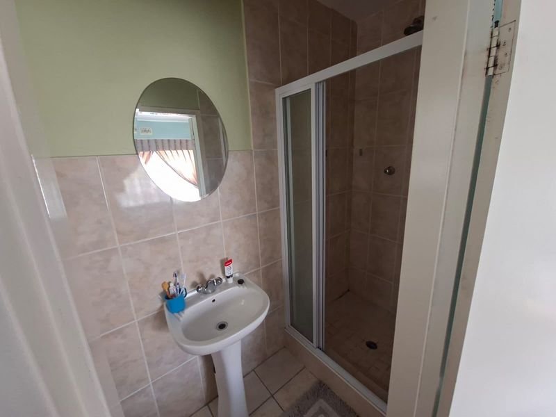 A functional bathroom featuring a pedestal basin, tiled walls, and a glass-enclosed shower unit.