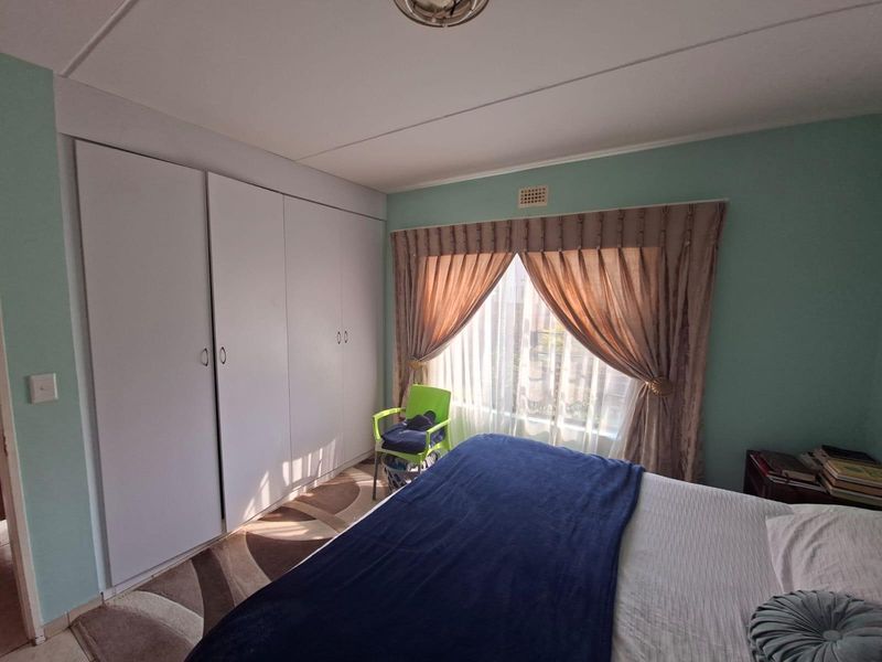 A bedroom featuring built-in cupboards and a window with curtain rails, providing functional storage and natural light.