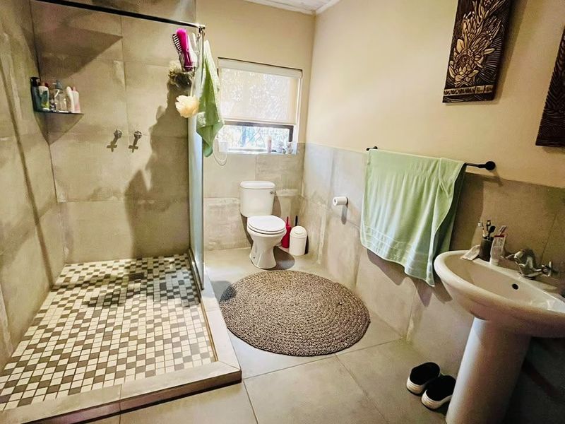 A functional bathroom featuring a walk-in shower with mosaic floor tiles, a pedestal basin, and a toilet, finished with neutral wall tiles.
