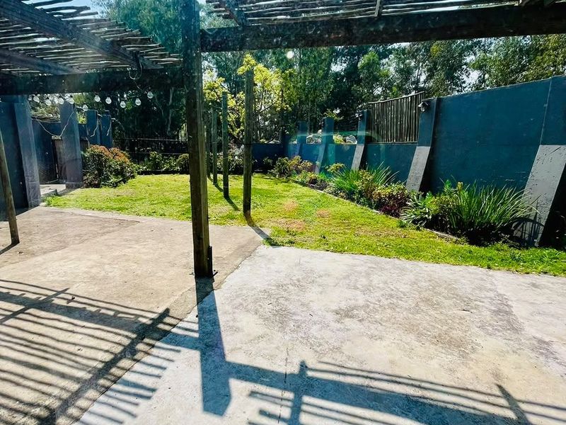 Outdoor patio area featuring a wooden pergola structure, concrete flooring, and a private garden space with boundary walls.