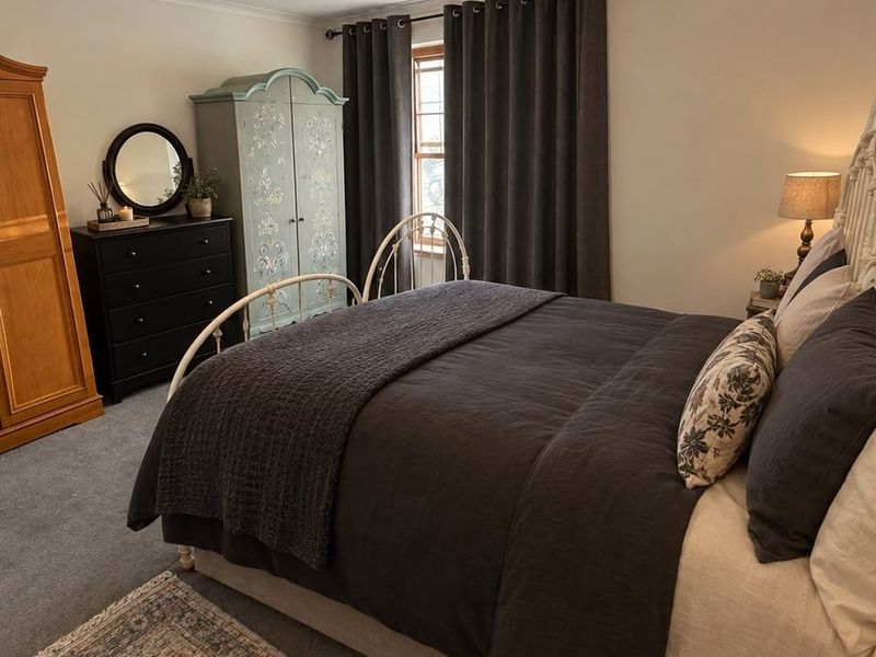 A well-maintained bedroom featuring neutral walls, carpeted flooring, and a window with dark curtains.