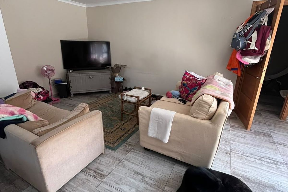 A living room area featuring tiled flooring and coved ceilings, currently showing signs of wear on the walls and ceiling.