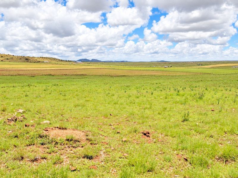 A wide-angle view of expansive, open grassland with distant hills and wire fencing, showcasing the natural landscape of the vacant residential property.