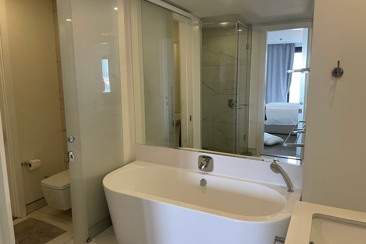 Modern bathroom featuring a sleek freestanding bathtub, wall-mounted toilet, glass-enclosed shower, and large vanity mirror with contemporary finishes.