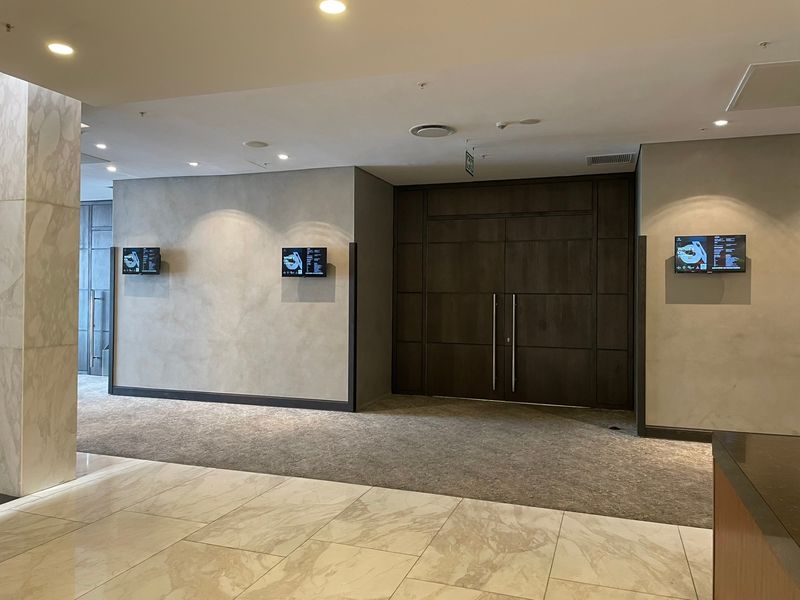 A modern, well-maintained building entrance lobby featuring marble flooring, recessed lighting, and double timber doors with integrated digital information displays.