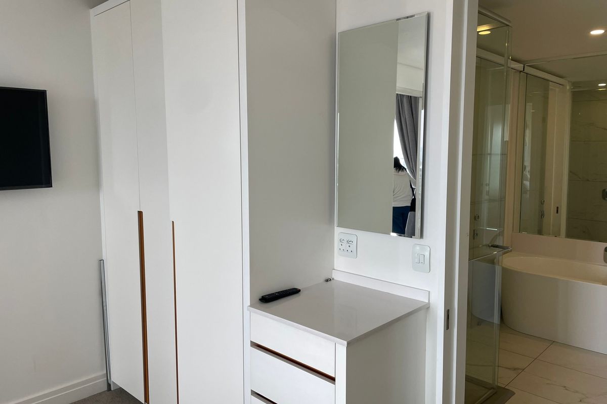 Modern bedroom featuring a sleek built-in wardrobe and a compact vanity area with integrated storage, adjacent to an en-suite bathroom.