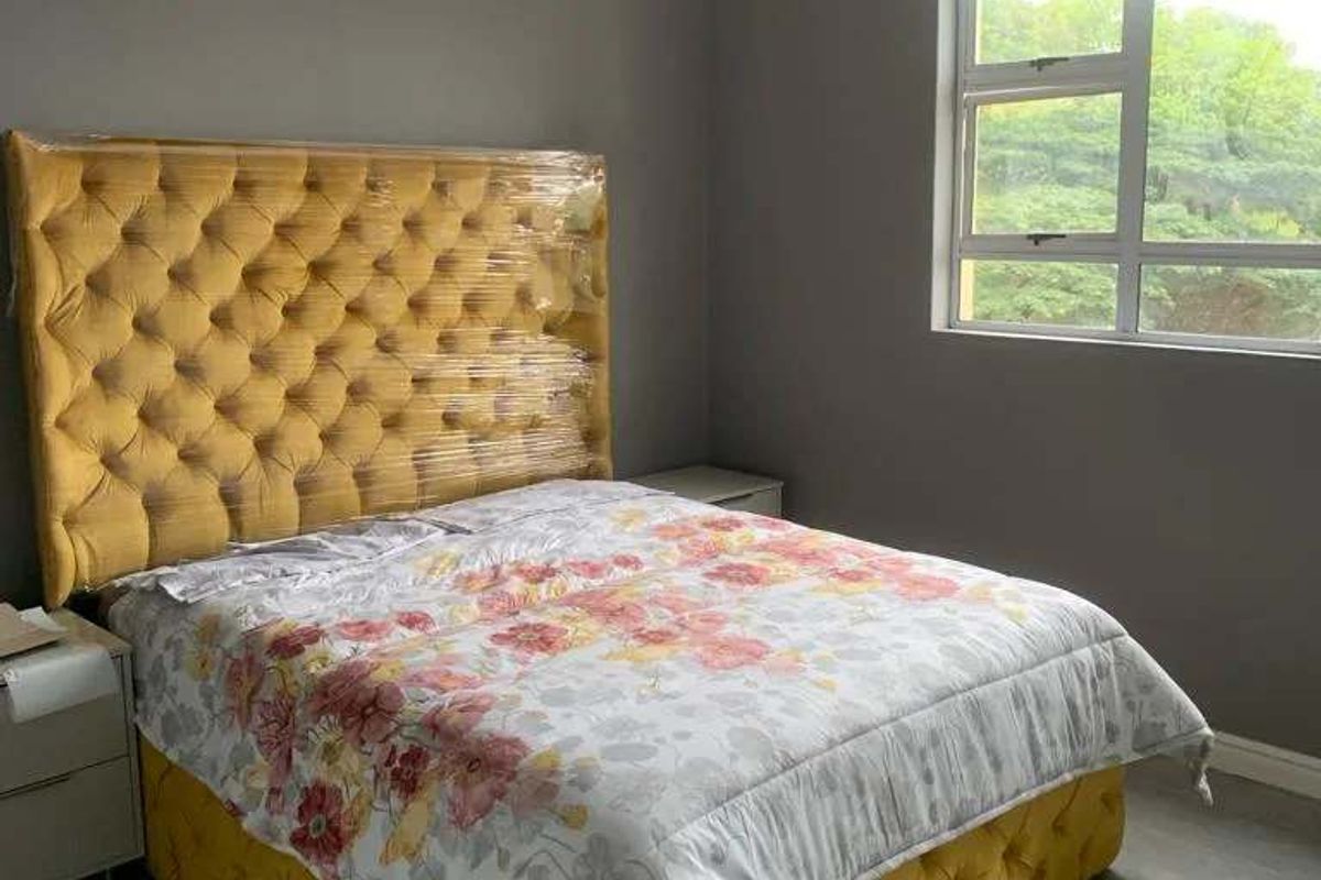 A well-maintained bedroom featuring neutral grey walls, tiled flooring, and a large window providing natural light and a green outlook.