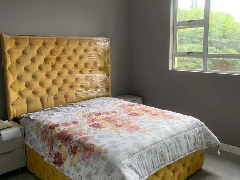 A well-maintained bedroom featuring neutral grey walls, tiled flooring, and a large window providing natural light and a green outlook.