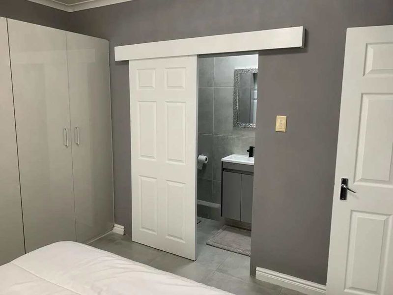 A modern bedroom featuring grey walls, built-in cupboards, and a white sliding barn door providing access to an en-suite bathroom.