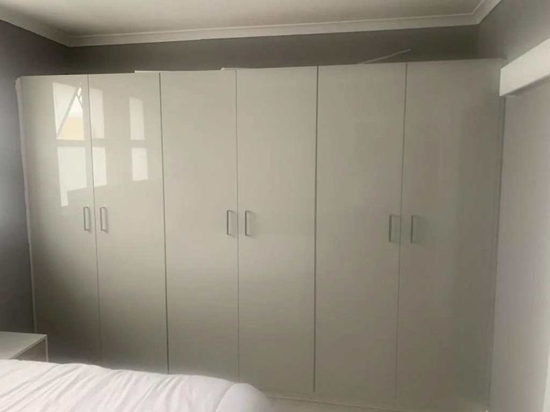 A bedroom featuring modern, floor-to-ceiling built-in cupboards with a clean, neutral finish.