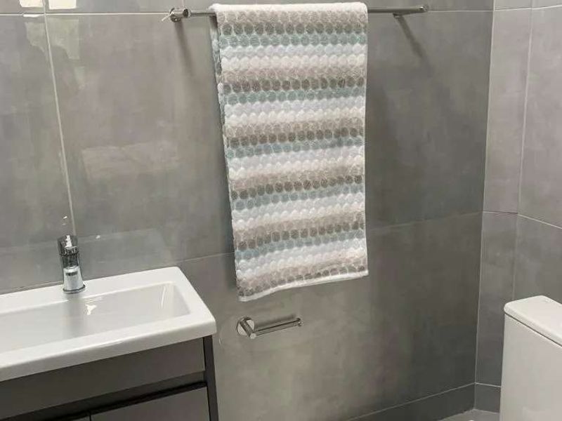 A modern bathroom featuring grey wall tiles, a sleek vanity cabinet with a basin, and a white toilet.