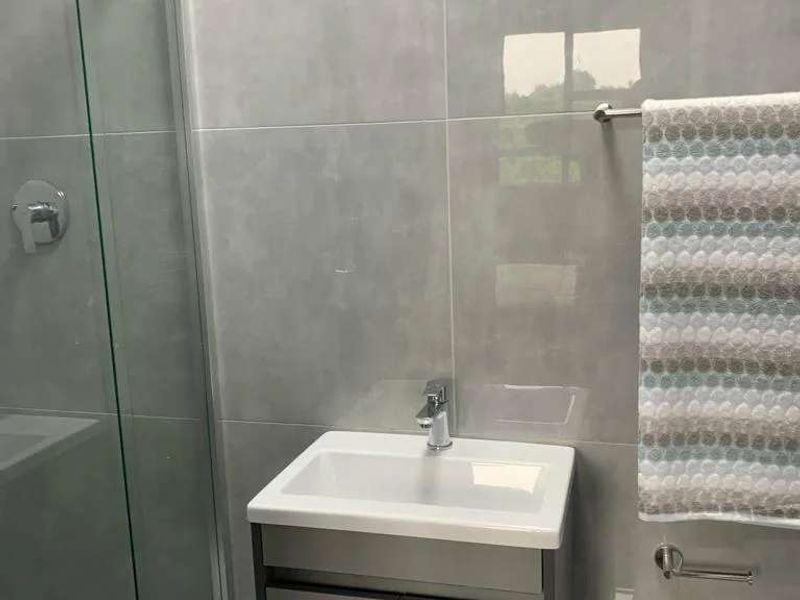 Modern bathroom featuring a glass shower enclosure, sleek vanity cabinet with integrated basin, and contemporary grey wall tiling.