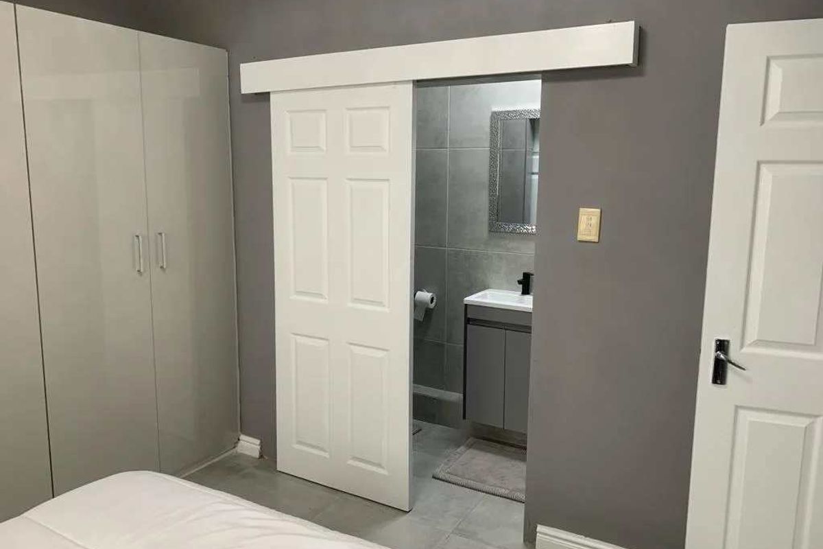 A modern bedroom featuring grey walls, built-in cupboards, and a white sliding barn door providing access to an en-suite bathroom.