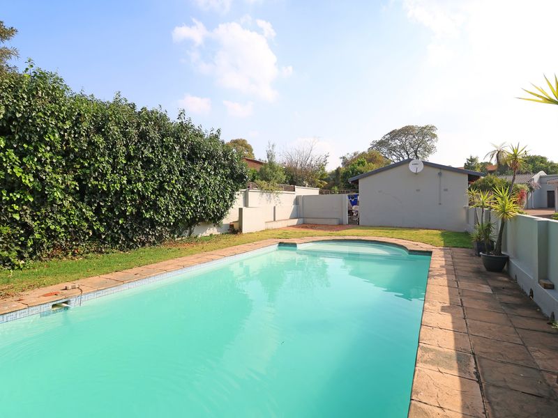 A private outdoor pool area featuring a swimming pool with paved surround, enclosed by boundary walls and established garden greenery.