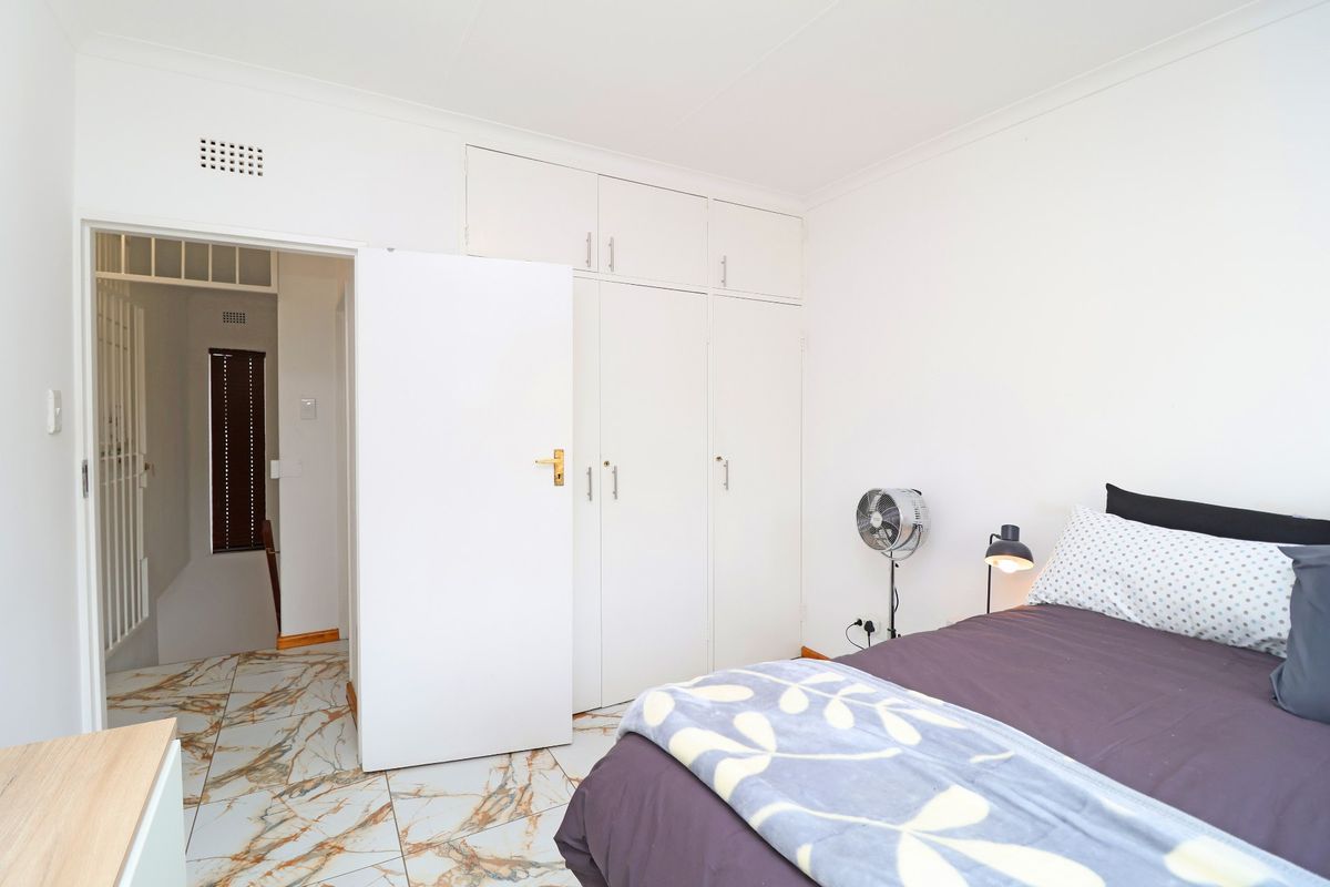 A bright bedroom featuring built-in cupboards and modern marble-effect tiled flooring, providing a clean and functional living space.