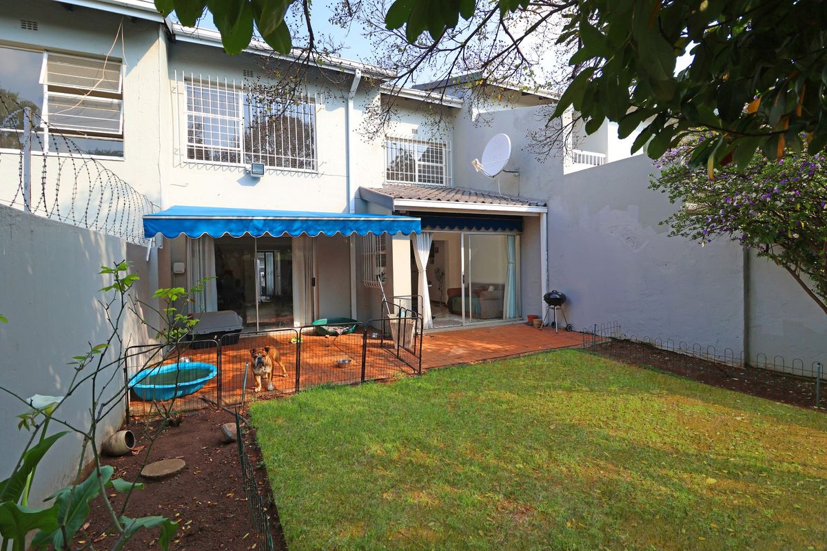 Rear view of the townhouse featuring a tiled patio, retractable awning, sliding glass doors, and a private garden area with boundary walls.