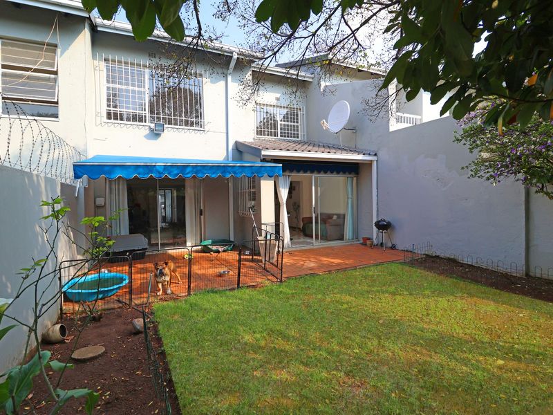 Rear view of the townhouse featuring a tiled patio, retractable awning, sliding glass doors, and a private garden area with boundary walls.
