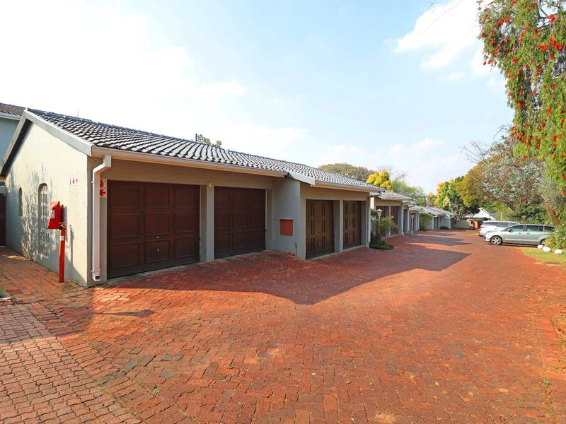 A row of residential garages featuring dark wood-style doors, tiled roofing, and a spacious brick-paved driveway area.