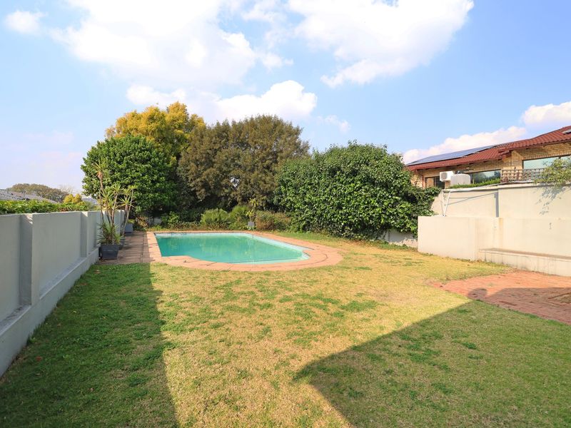 A private backyard featuring a swimming pool, paved surround, and a lawn area enclosed by boundary walls.