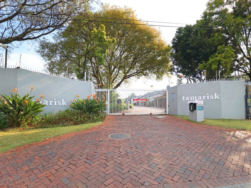 The secure entrance to Tamarisk complex featuring a paved driveway, automated security gate, intercom system, and perimeter boundary walls with electric fencing.
