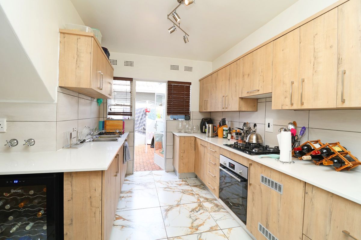 Modern galley-style kitchen featuring light wood-grain cabinetry, white countertops, marble-look floor tiles, and integrated appliances including a gas hob and oven.
