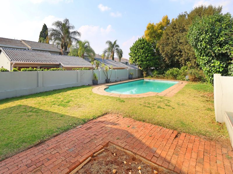 A private backyard featuring a swimming pool, brick-paved patio area, and a surrounding lawn enclosed by a boundary wall.