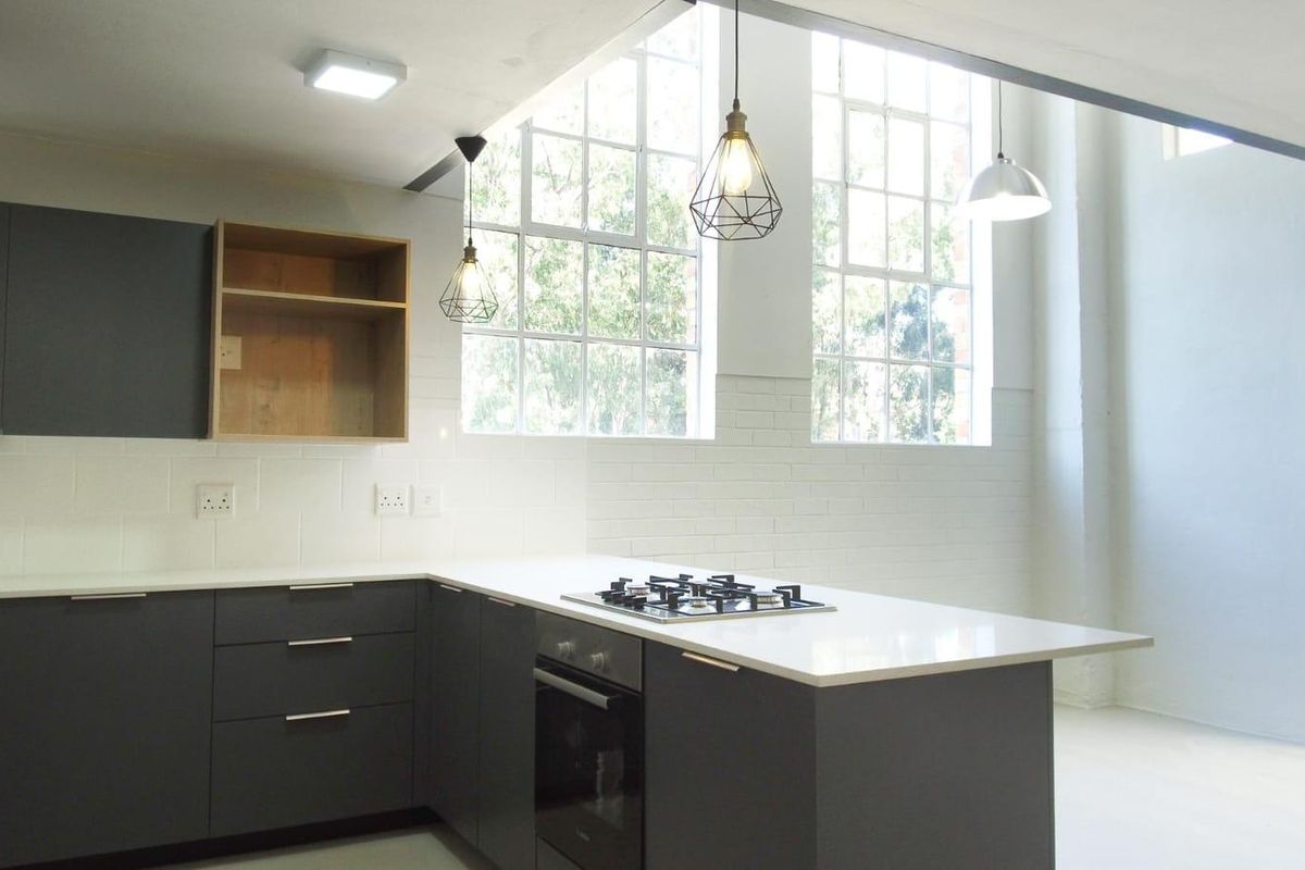 Modern kitchen featuring dark cabinetry, quartz countertops, built-in oven, gas hob, and large industrial-style windows providing ample natural light.