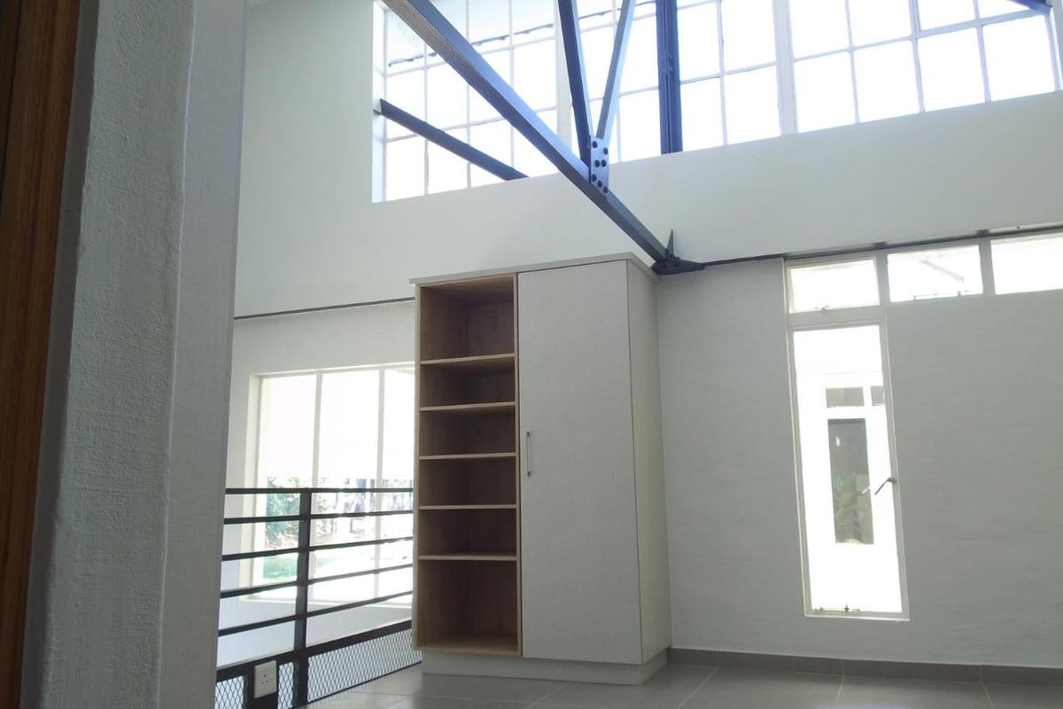 Spacious living area featuring high ceilings with exposed steel trusses, large industrial windows, and a modern built-in shelving unit.