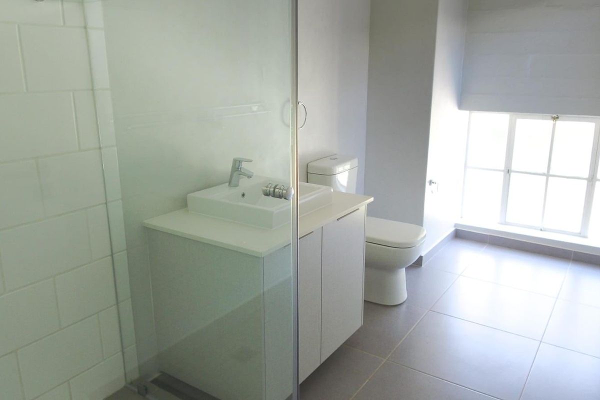 A clean, modern bathroom featuring a glass-enclosed shower, vanity with basin, and toilet, finished with neutral floor tiles and white subway wall tiles.