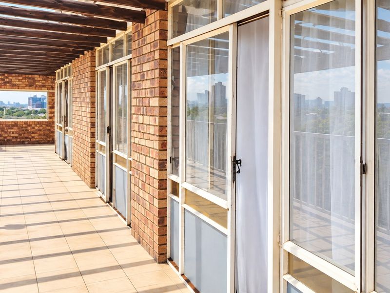Spacious covered balcony featuring a brick facade, tiled flooring, and multiple sliding glass doors with views of the surrounding cityscape.