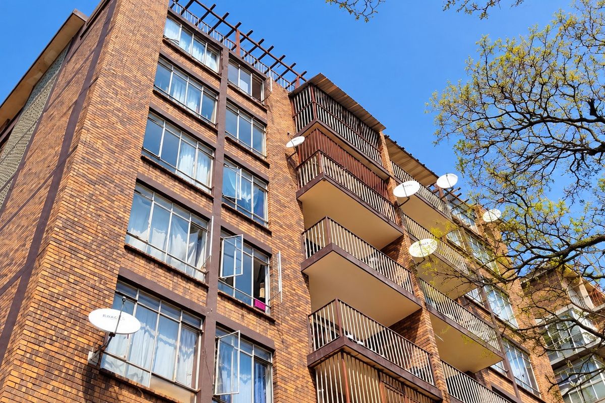 Low-angle view of a multi-story brick apartment building featuring private balconies with metal railings and multiple satellite dishes.