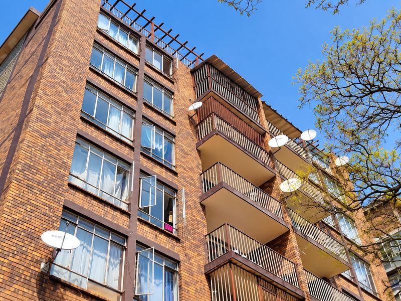 Low-angle view of a multi-story brick apartment building featuring private balconies with metal railings and multiple satellite dishes.