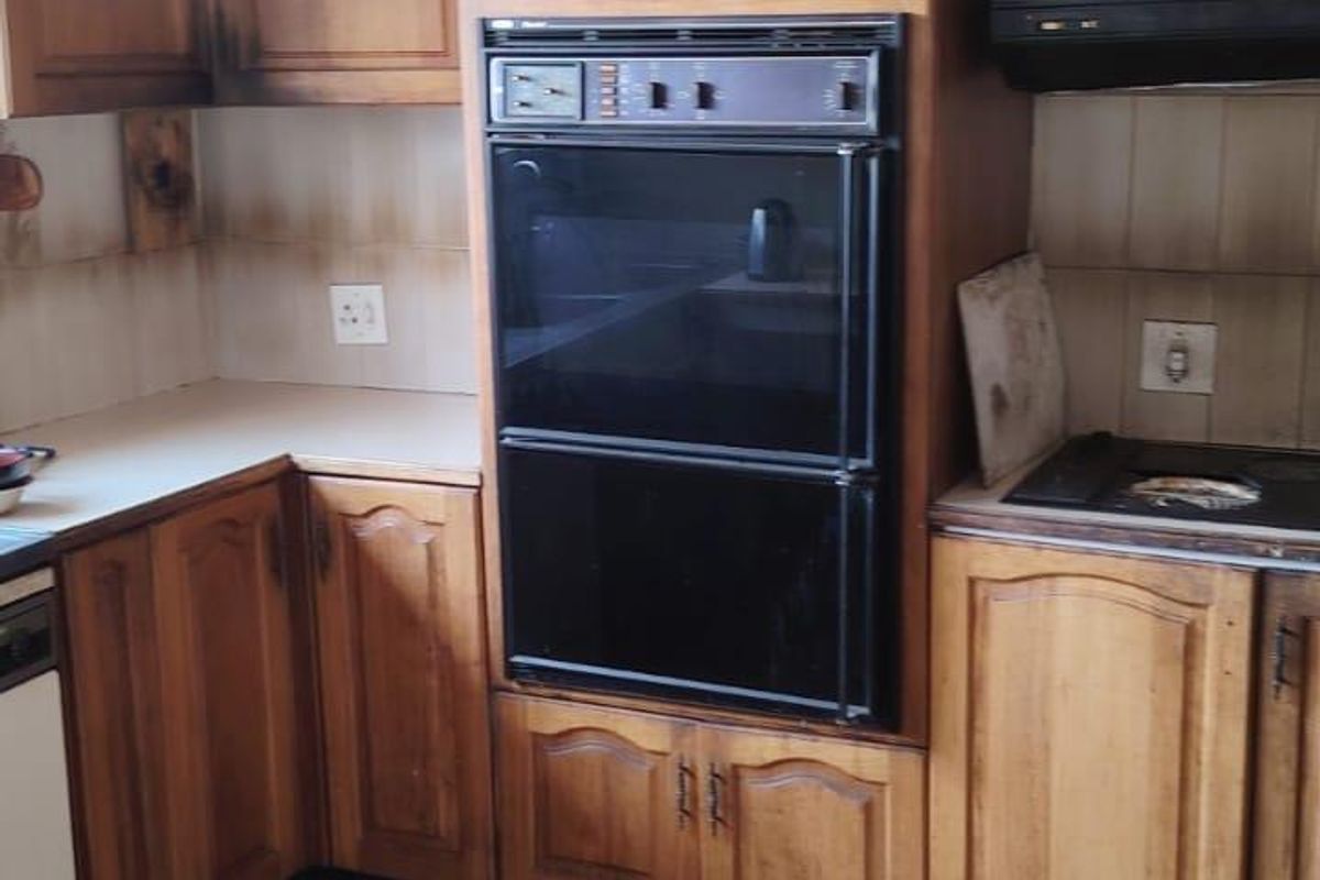 A dated kitchen featuring wooden cabinetry, a built-in double oven, and tiled flooring, offering significant potential for modernization and renovation.