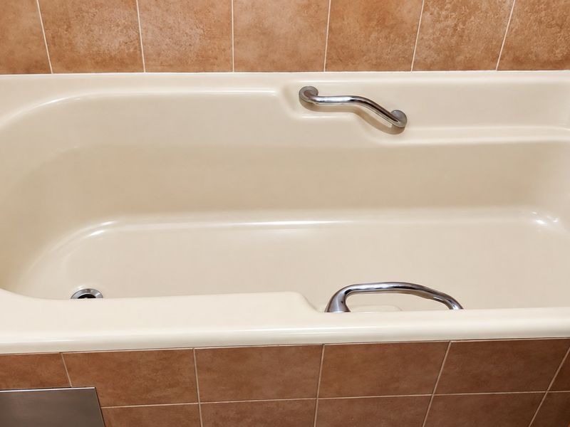 A standard bathroom featuring a built-in bathtub with chrome fixtures and grab bars, finished with neutral-toned ceramic wall tiling.