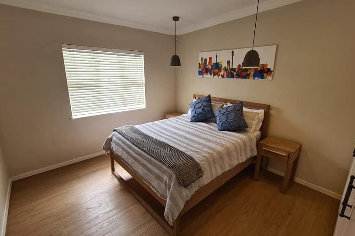 A well-maintained bedroom featuring laminate flooring, neutral wall tones, built-in cupboards, and modern pendant lighting.
