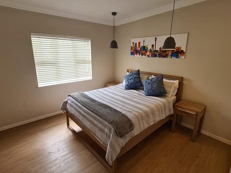 A well-maintained bedroom featuring laminate flooring, neutral wall tones, built-in cupboards, and modern pendant lighting.