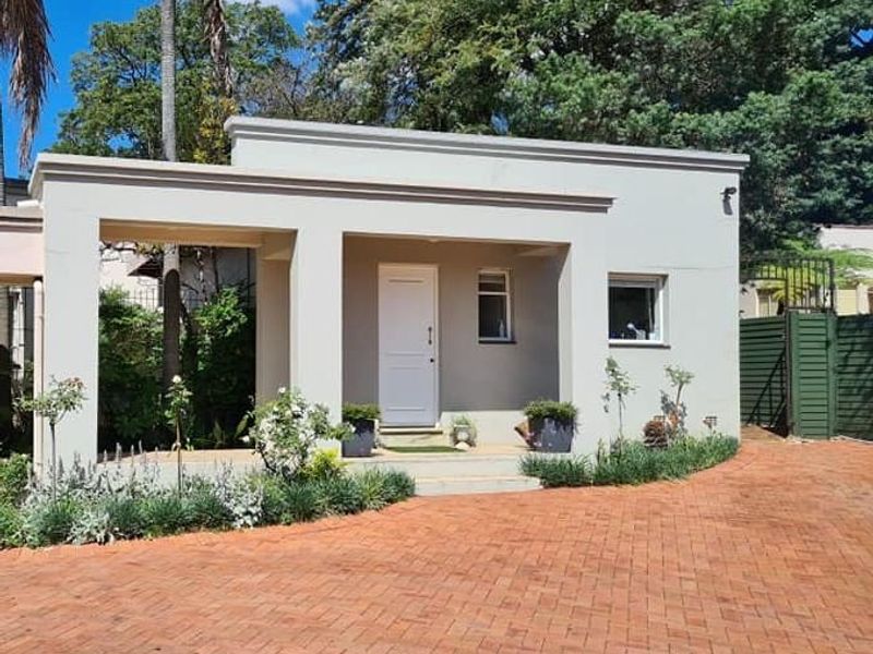 Front elevation of a single-story home featuring a covered porch entrance and a brick-paved driveway set within a landscaped garden.