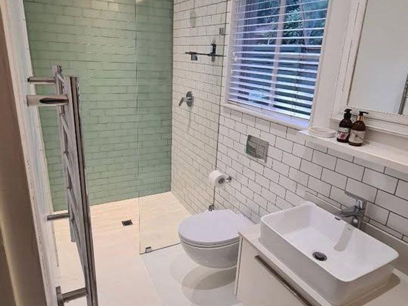 Modern bathroom featuring a walk-in shower with green subway tiles, wall-mounted toilet, vessel sink vanity, and a heated towel rail.