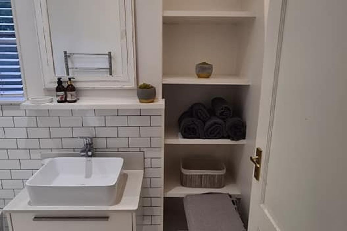 A modern bathroom featuring a vessel sink, wall-mounted vanity, subway tile backsplash, and convenient built-in shelving for storage.