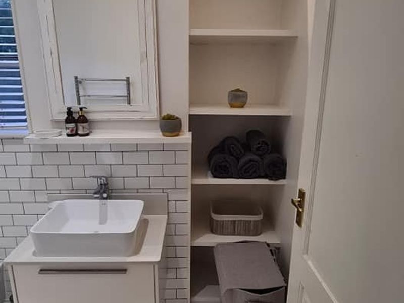 A modern bathroom featuring a vessel sink, wall-mounted vanity, subway tile backsplash, and convenient built-in shelving for storage.
